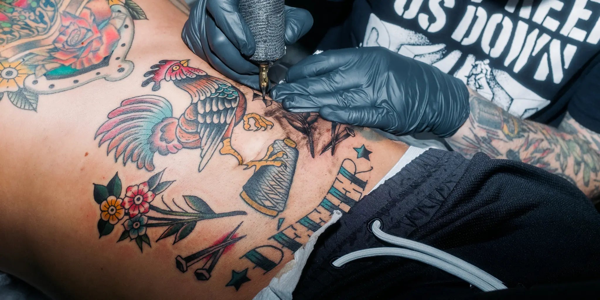 Rooster tattoo with Défier lettering on the stomach of a team member of our fashion brand.