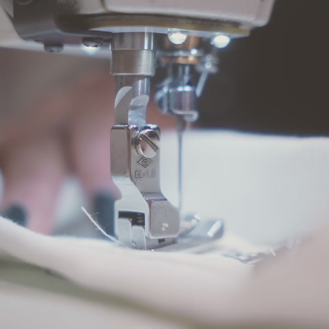 Video of a sewing machine sewing a Défier neck label onto an oversized T-shirt.